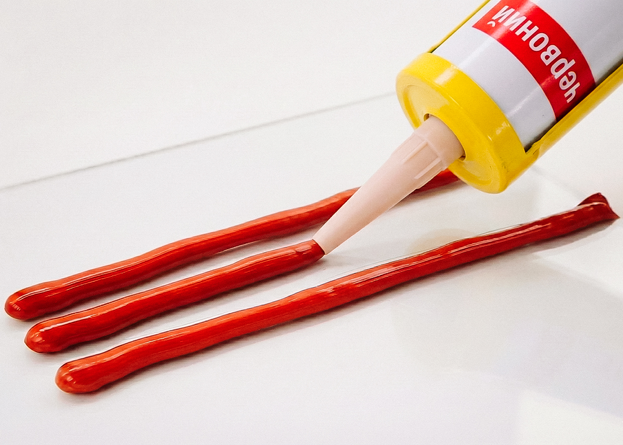 Нанесение красного высокотемпературного герметика из тубы на белую поверхность Нанесение красного высокотемпературного герметика из тубы на белую поверхность