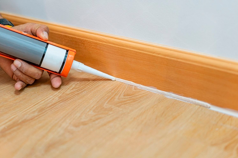 Пістолет для герметика наносить акриловий герметик уздовж стику підлоги і дерев’яного плінтуса